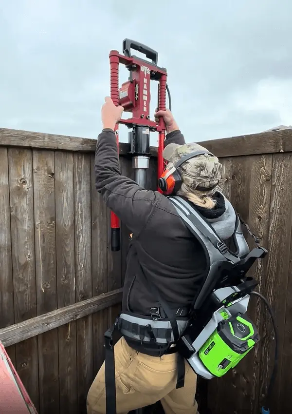 Rockwall Outdoor Living installer using professional equipment to drive a steel fence post for a residential fencing project in Rockwall, TX.